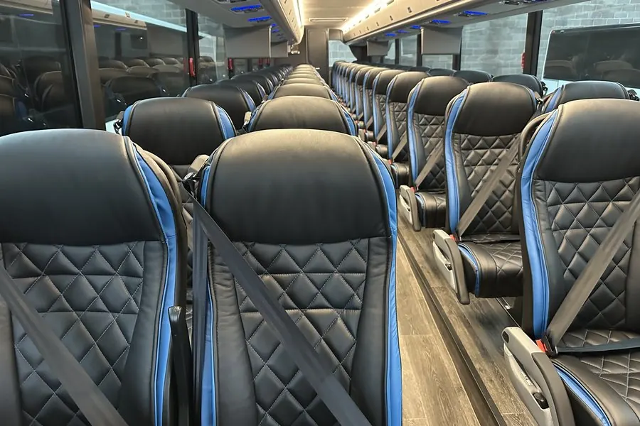 Motorcoach cabin with rows of black leather reclining seats trimmed in blue, looking down the centre aisle